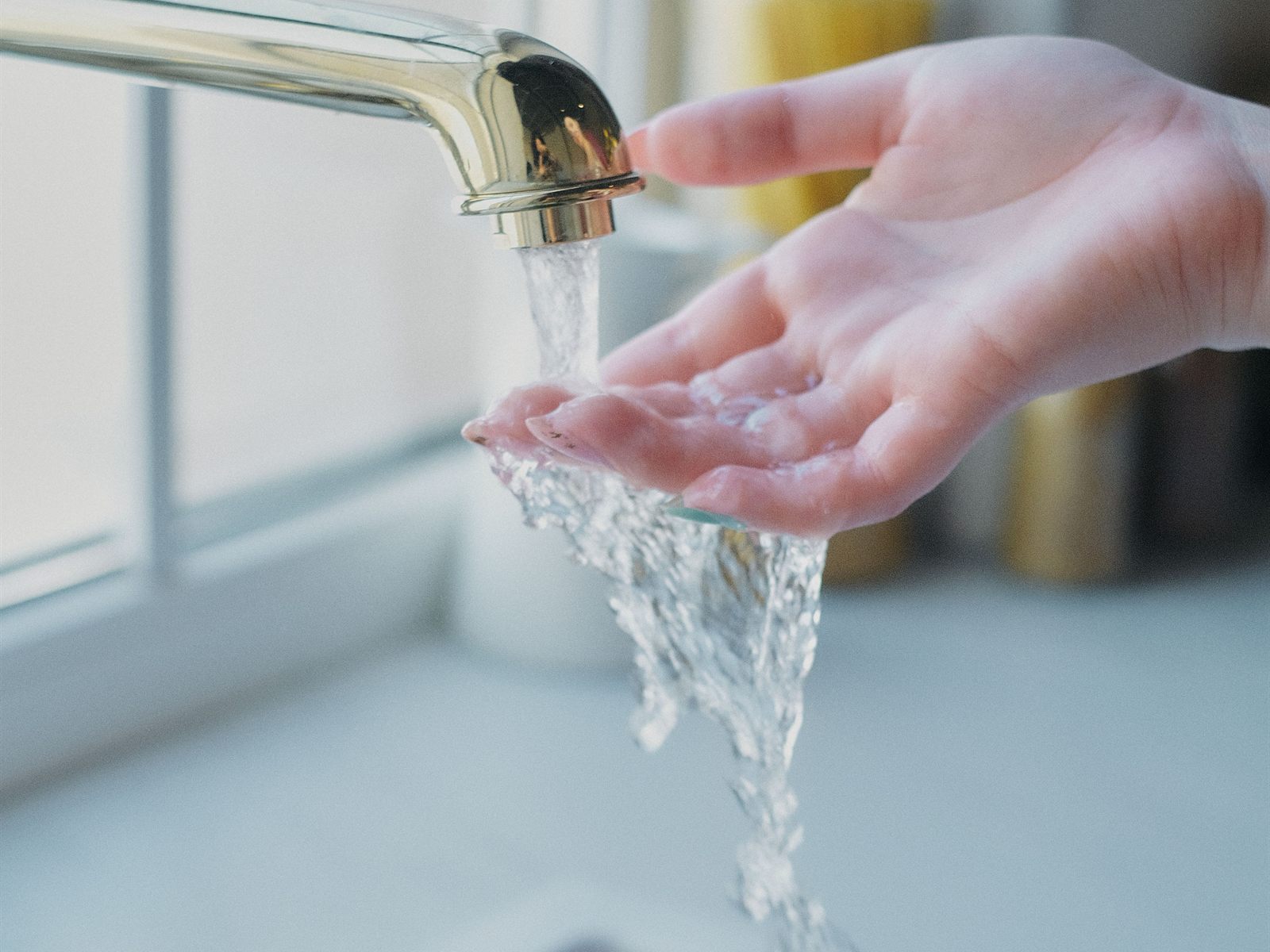 Clean water running from a brass kitchen faucet over a cupped hand