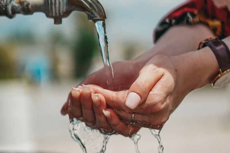 Hands cupped under an outdoor brass well tap